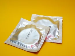 Dois preservativos em embalagens prateadas sobre um fundo amarelo.