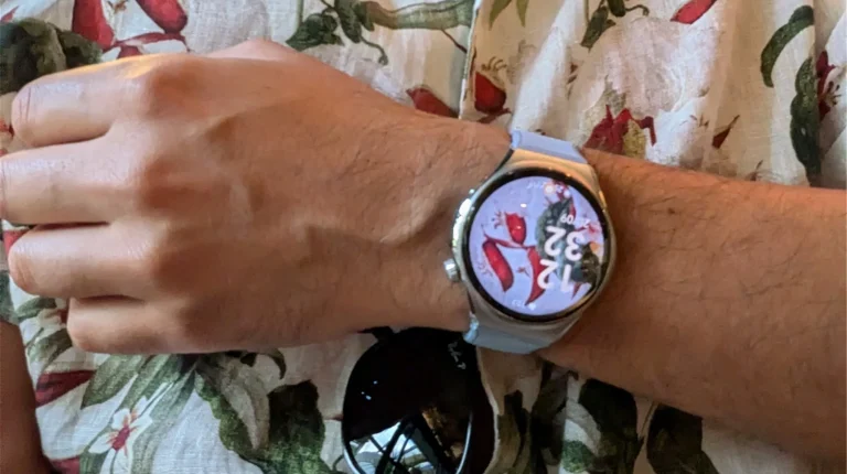 Smartwatch prateado no pulso sobre uma camisa floral.