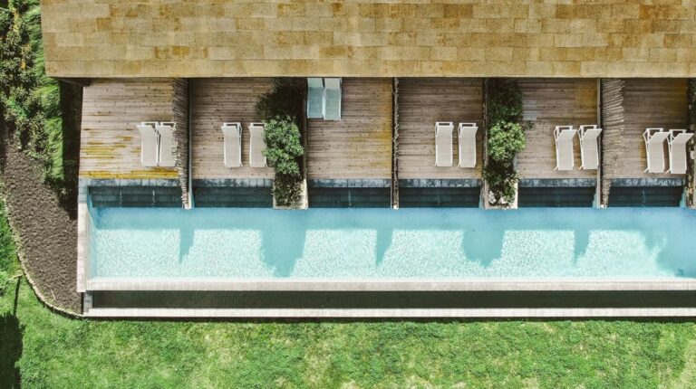 Vista aérea de piscina com espreguiçadeiras e jardim.