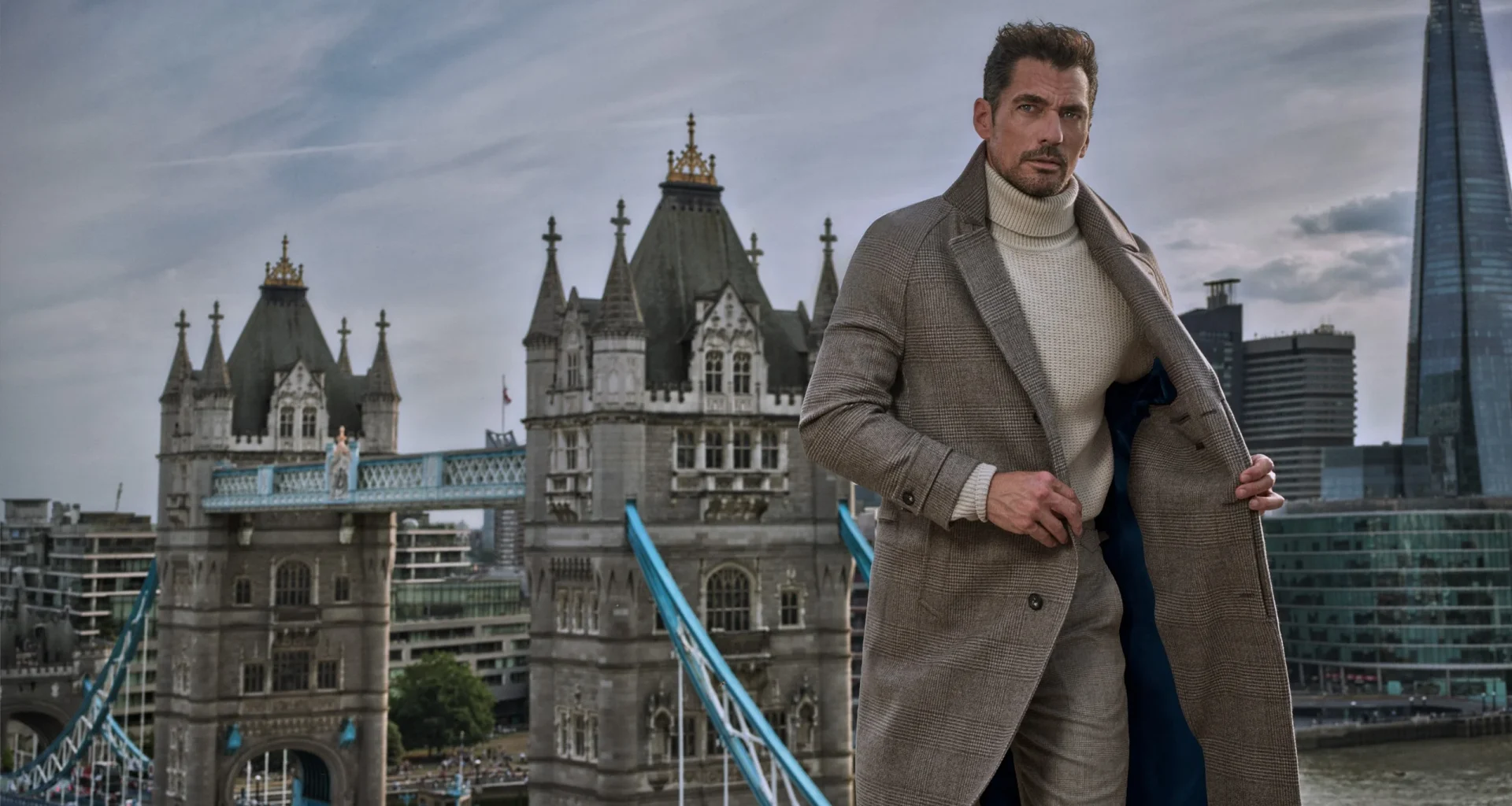 Homem elegante com sobretudo cinzento perante a Tower Bridge.