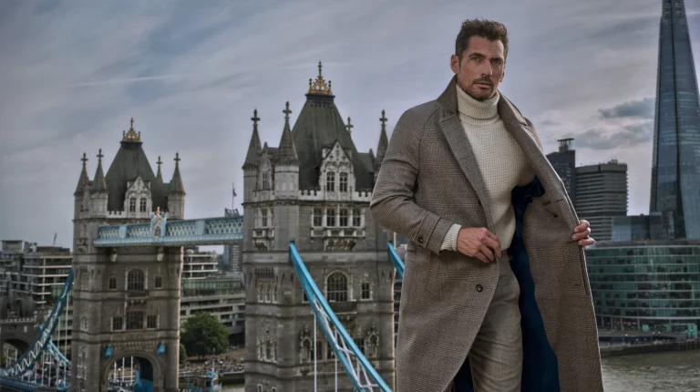 Homem elegante com sobretudo cinzento perante a Tower Bridge.