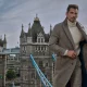 Homem elegante com sobretudo cinzento perante a Tower Bridge.