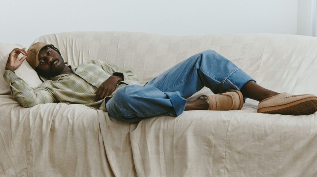 Homem jovem relaxando num sofá bege com roupa casual.