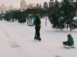 Pessoa de scooter puxa criança em trenó na neve.