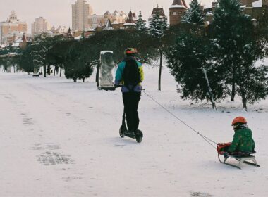 Pessoa de scooter puxa criança em trenó na neve.