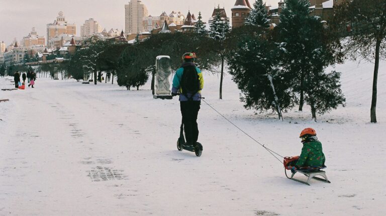 Pessoa de scooter puxa criança em trenó na neve.