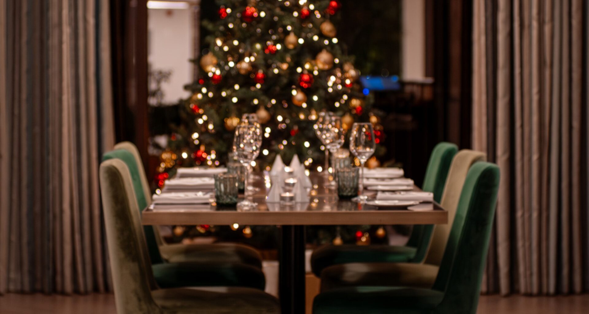 Mesa preparada para jantar de Natal, árvore ao fundo.