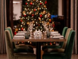 Mesa preparada para jantar de Natal, árvore ao fundo.