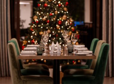 Mesa preparada para jantar de Natal, árvore ao fundo.