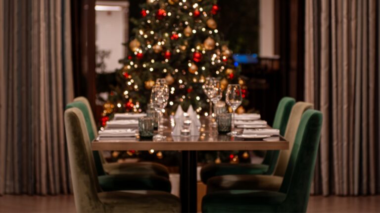 Mesa preparada para jantar de Natal, árvore ao fundo.