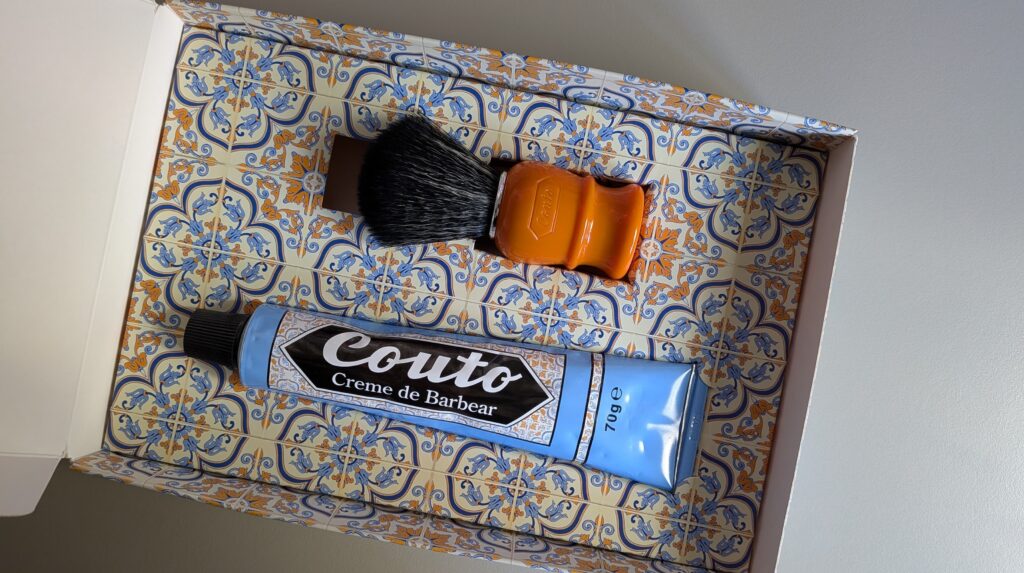 Caixa com padrão de azulejos portugueses contendo um pincel laranja e um tubo azul de creme de barbear Couto para evitar pelos encravados no pescoço.