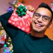 Homem sorrindo segurando presente natalino decorado.