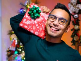 Homem sorrindo segurando presente natalino decorado.