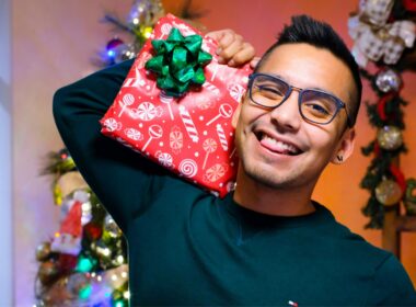 Homem sorrindo segurando presente natalino decorado.