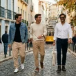 Três homens sorridentes caminham por rua típica de Lisboa.