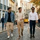Três homens sorridentes caminham por rua típica de Lisboa.