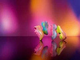 Quatro sapatilhas desportivas coloridas em superfície refletora, fundo vibrante.
