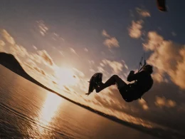 Atleta a praticar kitesurf com um salto de grande altitude ao pôr do sol nas Ilhas Canárias para ilustrar a procura constante de adrenalina