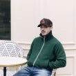 Homem de boné e casaco verde sentado em esplanada parisiense.