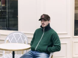 Homem de boné e casaco verde sentado em esplanada parisiense.