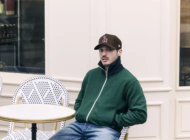 Homem de boné e casaco verde sentado em esplanada parisiense.