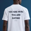 Homem com t-shirt branca "YOU ARE EATING" sobre fundo azul.