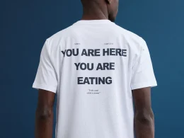 Homem com t-shirt branca "YOU ARE EATING" sobre fundo azul.