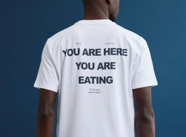 Homem com t-shirt branca "YOU ARE EATING" sobre fundo azul.