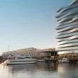 Marina com iates luxuosos e edifício moderno de vidro ondulado.