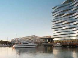 Marina com iates luxuosos e edifício moderno de vidro ondulado.