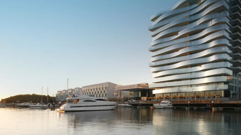 Marina com iates luxuosos e edifício moderno de vidro ondulado.
