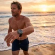 Homem a sair do mar numa praia ao pôr-do-sol.