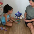 Homem e menina a jogar cartas no chão de madeira.