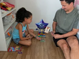Homem e menina a jogar cartas no chão de madeira.
