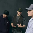 Três homens com bonés New Era num estilo streetwear urbano.