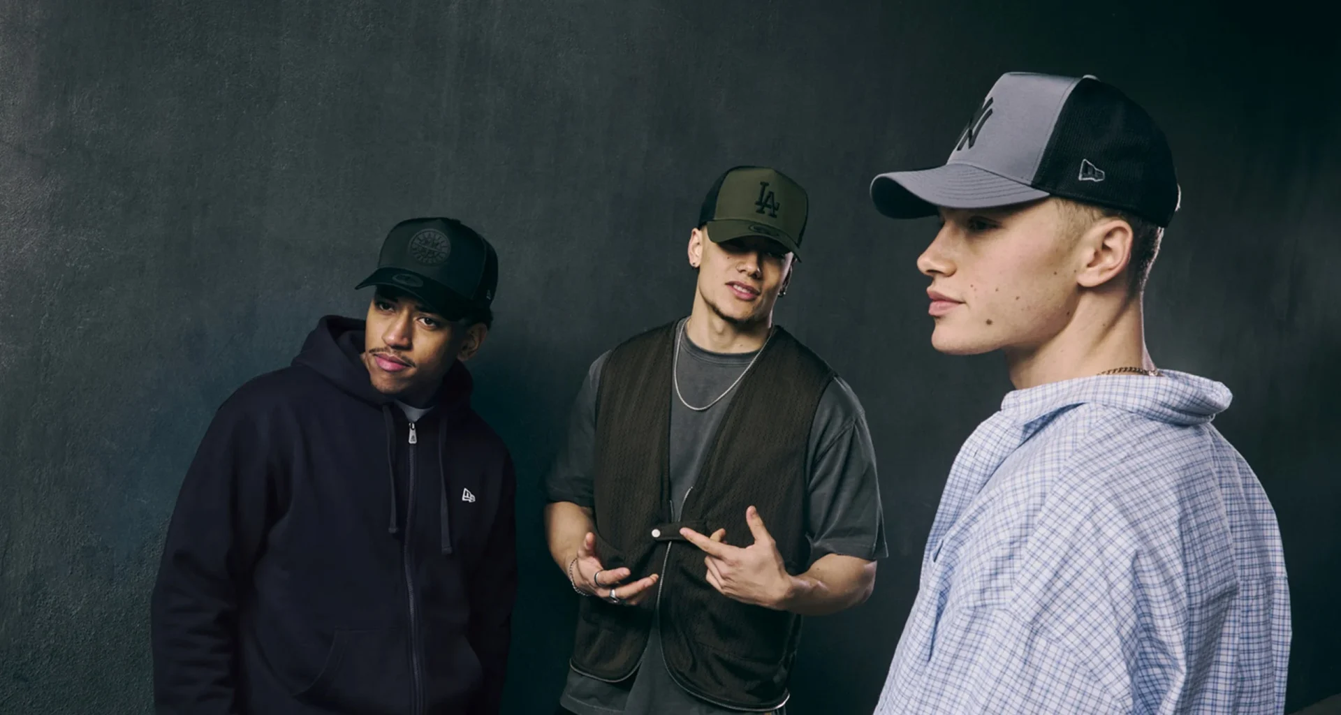 Três homens com bonés New Era num estilo streetwear urbano.