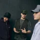 Três homens com bonés New Era num estilo streetwear urbano.