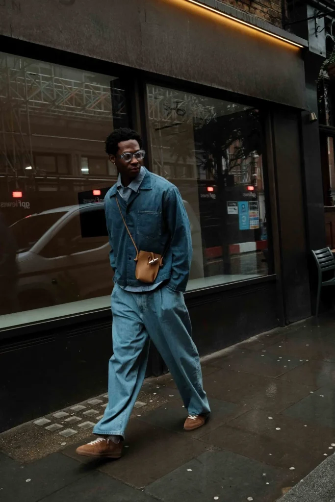 Homem, roupa ganga, óculos, mala castanha, rua urbana.