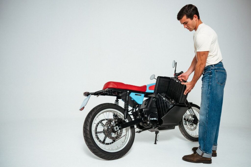 Homem carrega bateria de moto elétrica em estúdio.