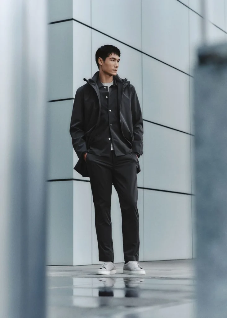 Homem com casaco e calças cinzentas.