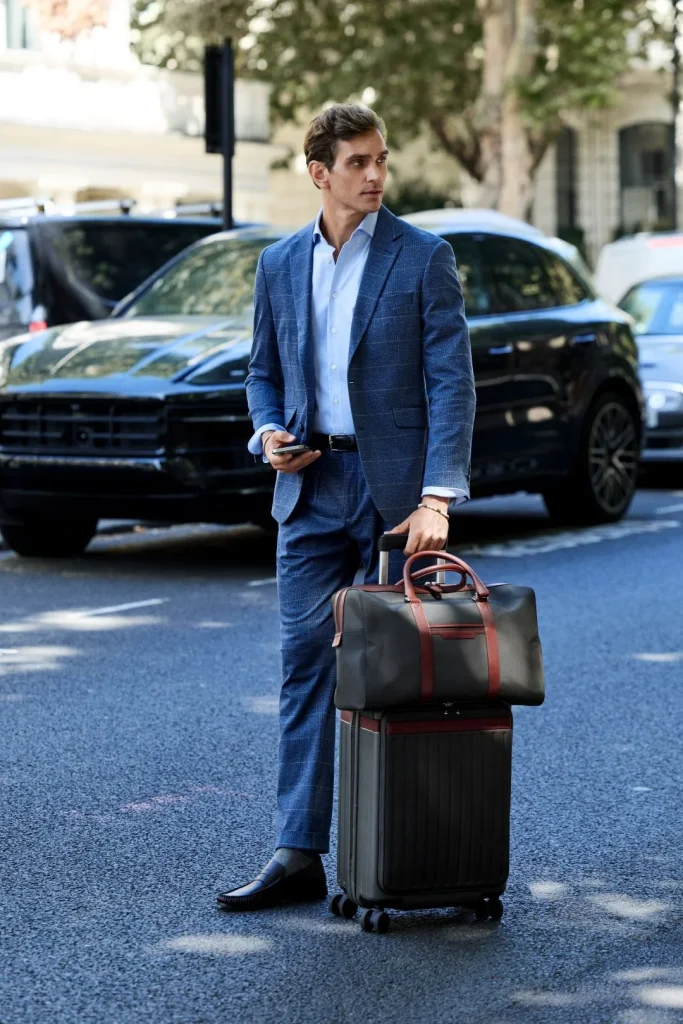 Homem veste fato azul xadrez da coleção Hackett London outono inverno com malas de viagem na rua
