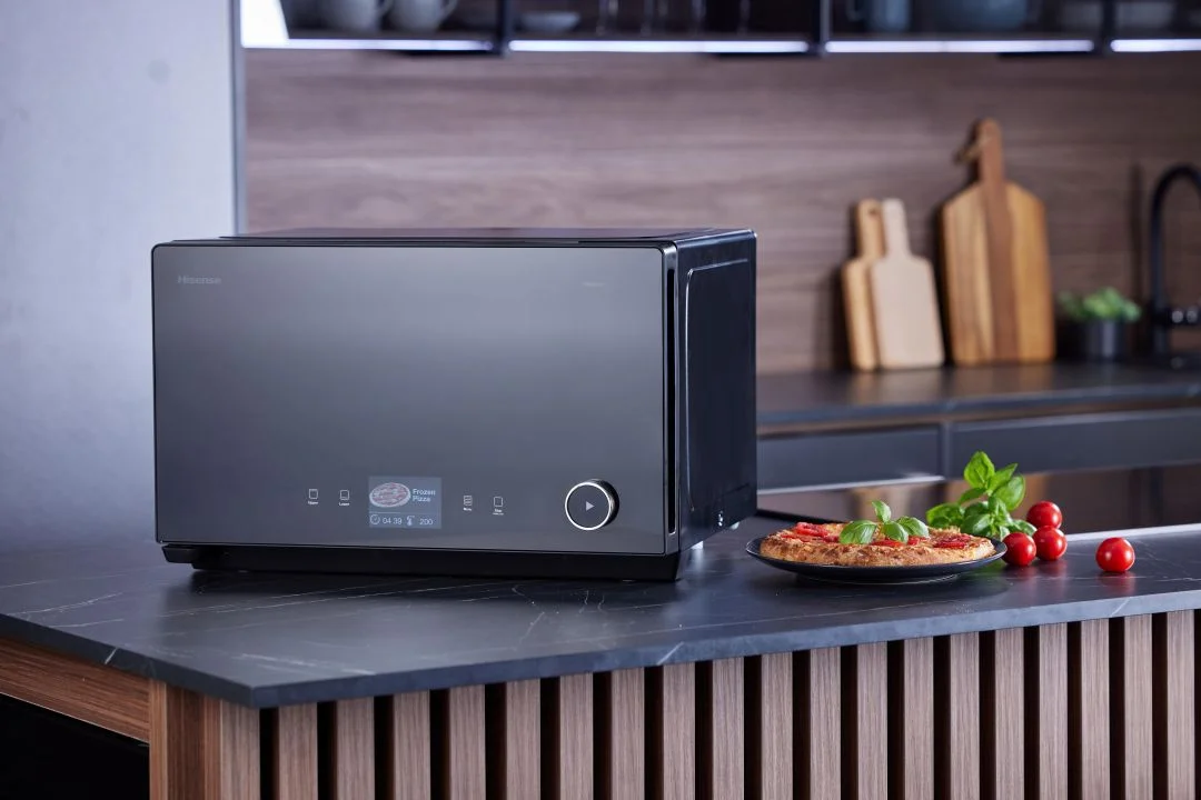 Forno inteligente preto da Hisense numa bancada de cozinha ao lado de uma pizza, exemplificando a inteligência artificial em casa.