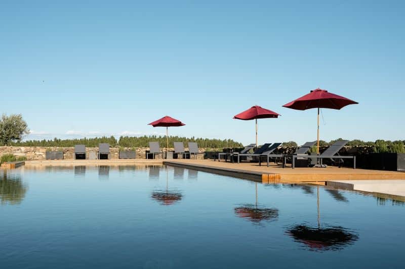 Piscina com espreguiçadeiras e chapéus de sol vermelhos.