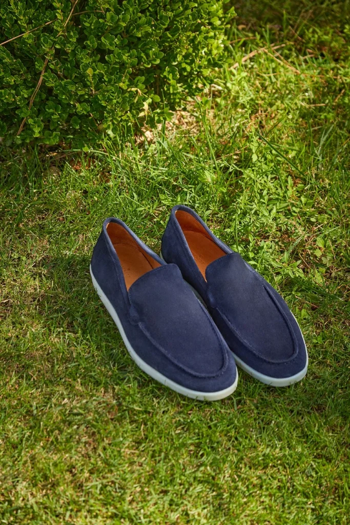 Mocassins de camurça azul sobre relva verde ao sol.