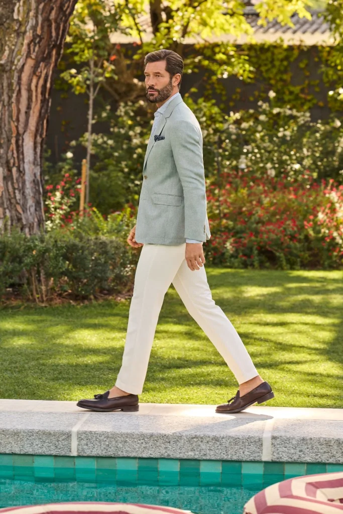 Homem elegante com blazer verde e calças brancas junto à piscina.