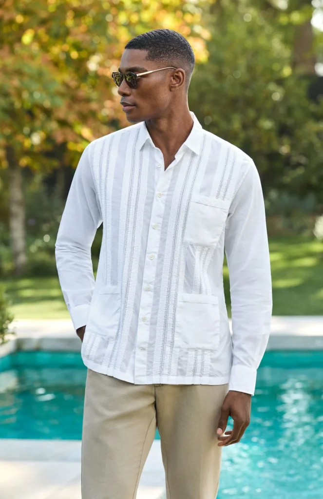 Homem de camisa branca guayabera e calças bege junto à piscina.
