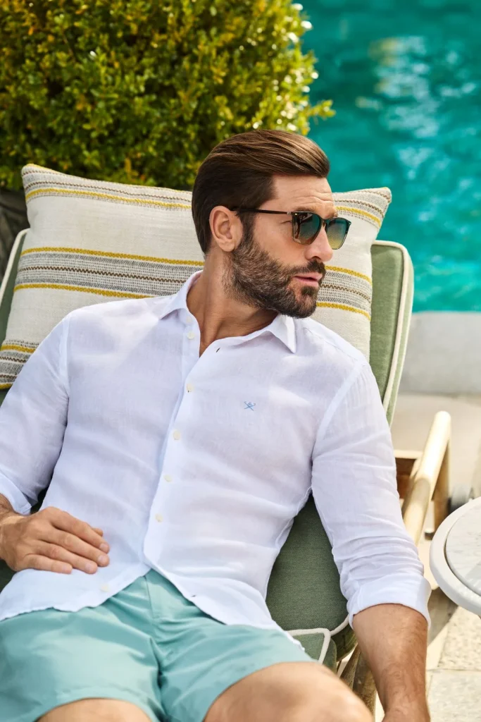 Homem com camisa de linho branca a relaxar na piscina.