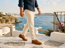 Homem caminha em terraço mediterrâneo com vista para o mar.