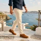 Homem caminha em terraço mediterrâneo com vista para o mar.