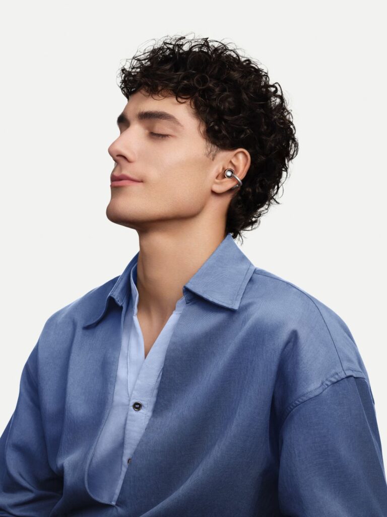 Homem com cabelo encaracolado a usar auriculares prateados abertos.